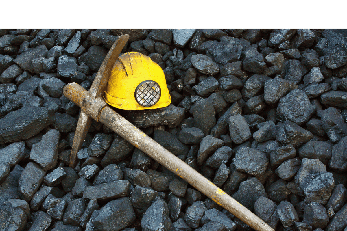 Pickaxe and yellow miner's helmet resting on a pile of black coal, symbolizing mining and resource extraction.