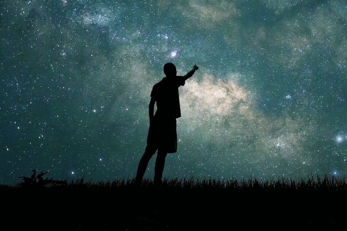 Silhouette of a person pointing at the starry night sky, symbolizing spiritual awakening, cosmic guidance, and connection to the universe.