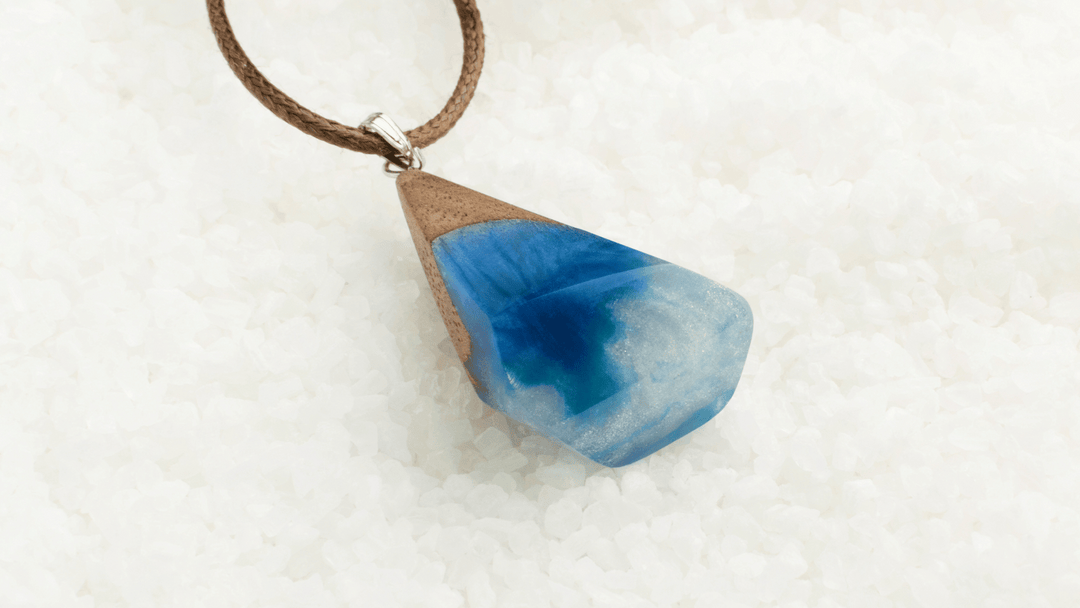 Handcrafted blue and white crystal pendant with wood accent on a brown cord, displayed on a bed of white Himalayan salt crystals.