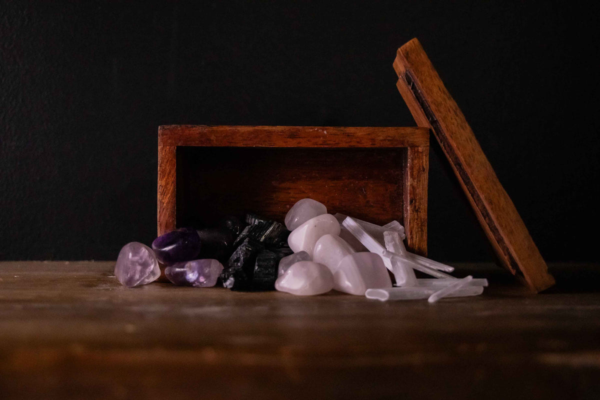 Tumbled amethyst, raw black tourmaline, rose quartz, and selenite crystals spilling from an open wooden box