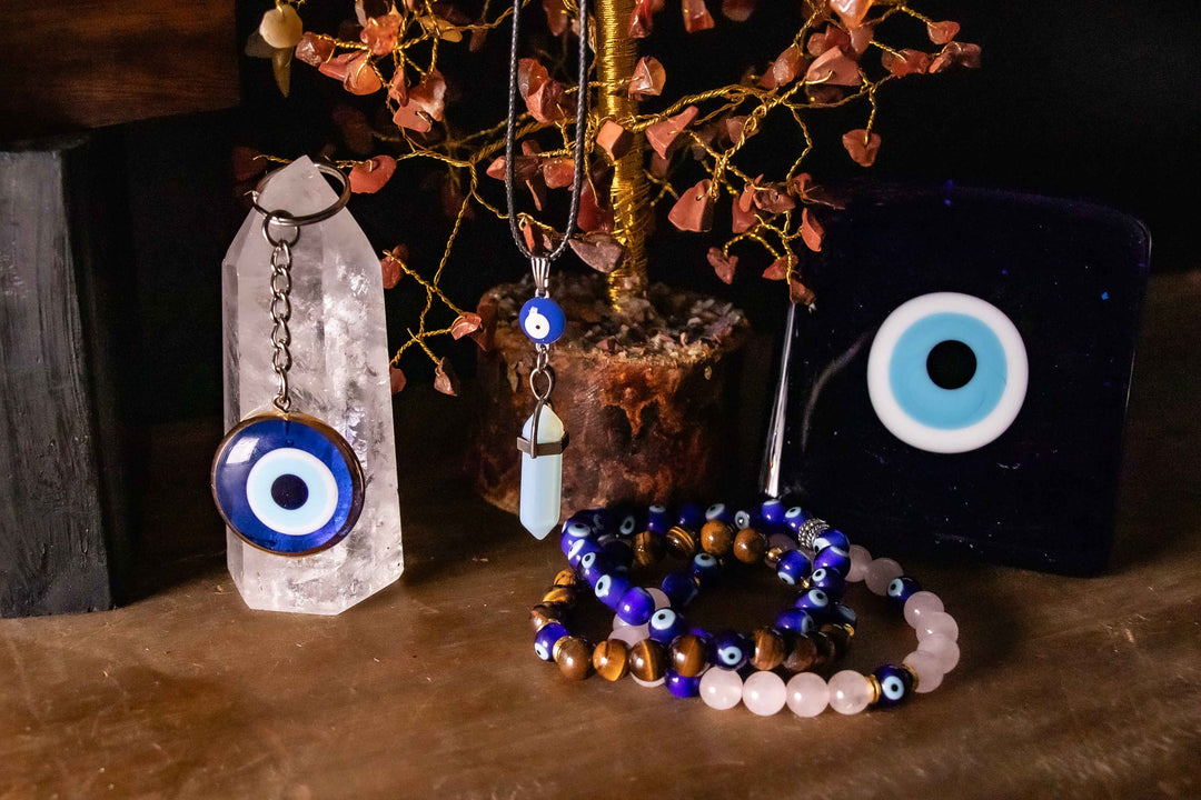 Evil eye protection collection including nazar keychain on clear quartz tower, opalite crystal point necklace, evil eye and tiger's eye bead bracelets, and large nazar wall talisman styled with a red jasper gemstone tree on a dark background