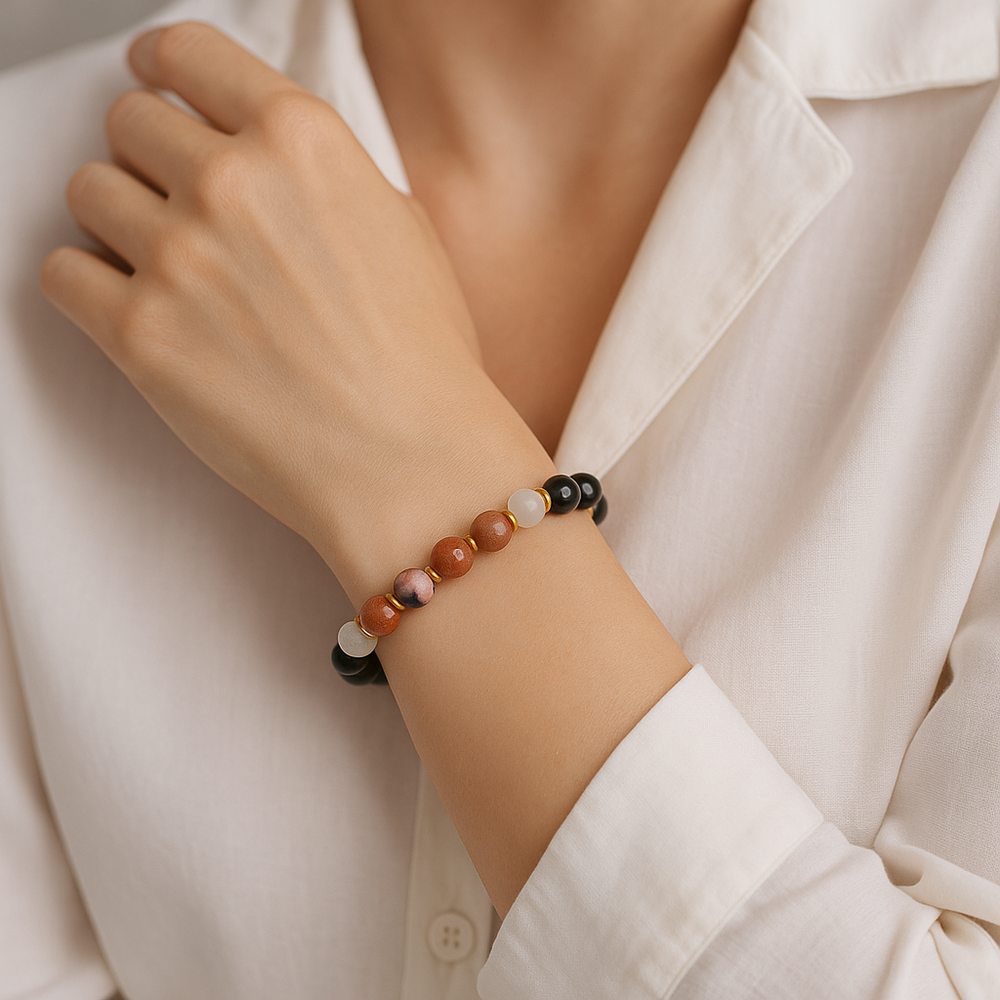 A woman's wrist adorned with a multi-bead bracelet featuring shiny black, smooth white, shimmering reddish-brown, and speckled pink beads separated by small gold rings