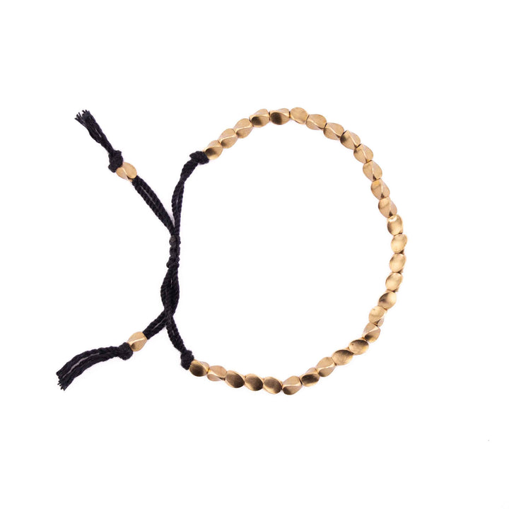 An adjustable bracelet featuring organic-shaped gold copper beads on a black braided cord with a sliding knot closure and tassel ends.