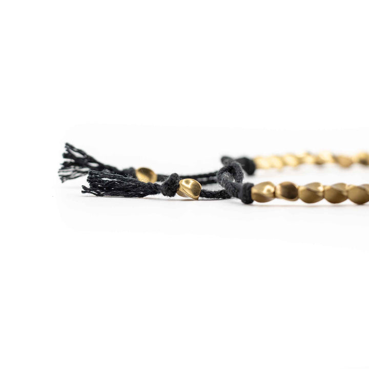 A close-up, low-angle shot of the black braided cord and gold copper beads, highlighting the tassel ends and sliding knot detail.