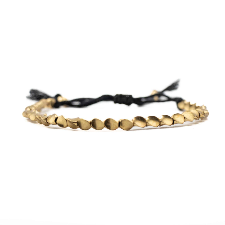 
A horizontal, eye-level view of the copper bead bracelet, focusing on the row of shiny, organic-shaped gold beads with the black cord and tassels blurred in the background.