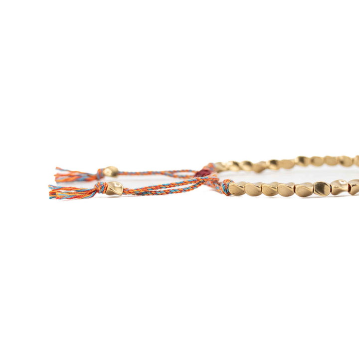 A close-up, low-angle shot of the multi-colored braided cord and gold copper beads, highlighting the tassel ends and sliding knot detail.
