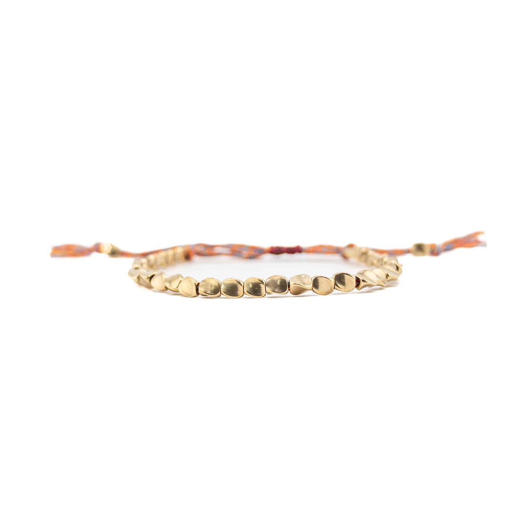 A horizontal, eye-level view of the copper bead bracelet, focusing on the row of shiny, organic-shaped gold beads with the multi-colored cord and tassels blurred in the background.