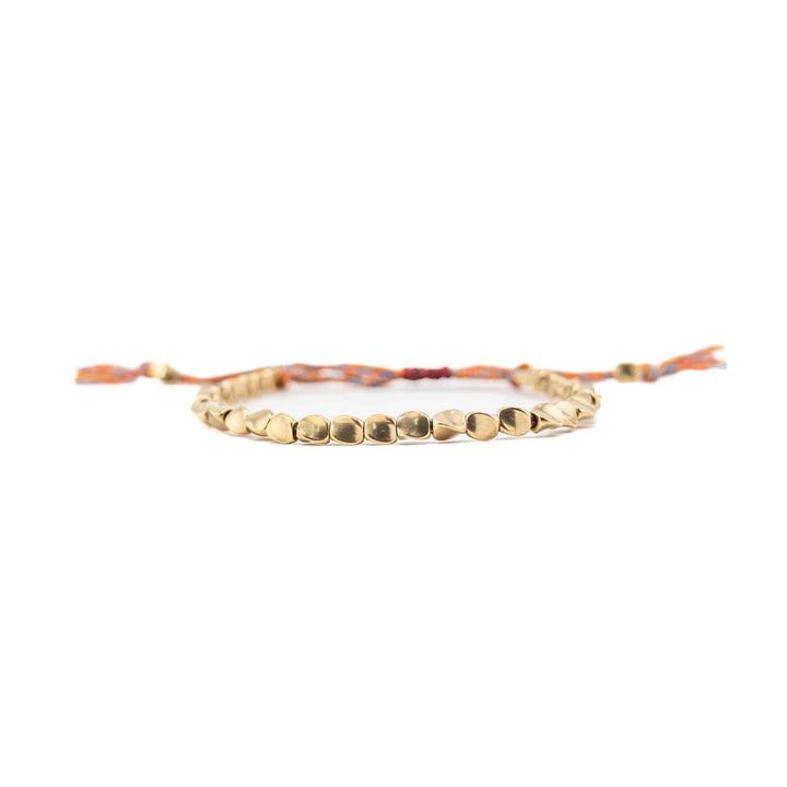 A horizontal, eye-level view of the copper bead bracelet, focusing on the row of shiny, organic-shaped gold beads with the multi-colored cord and tassels blurred in the background.
