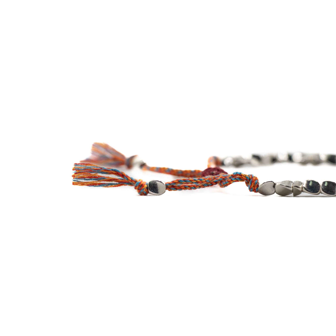 A close-up, low-angle shot of the multi-colored braided cord and silver copper beads, highlighting the tassel ends and sliding knot detail.