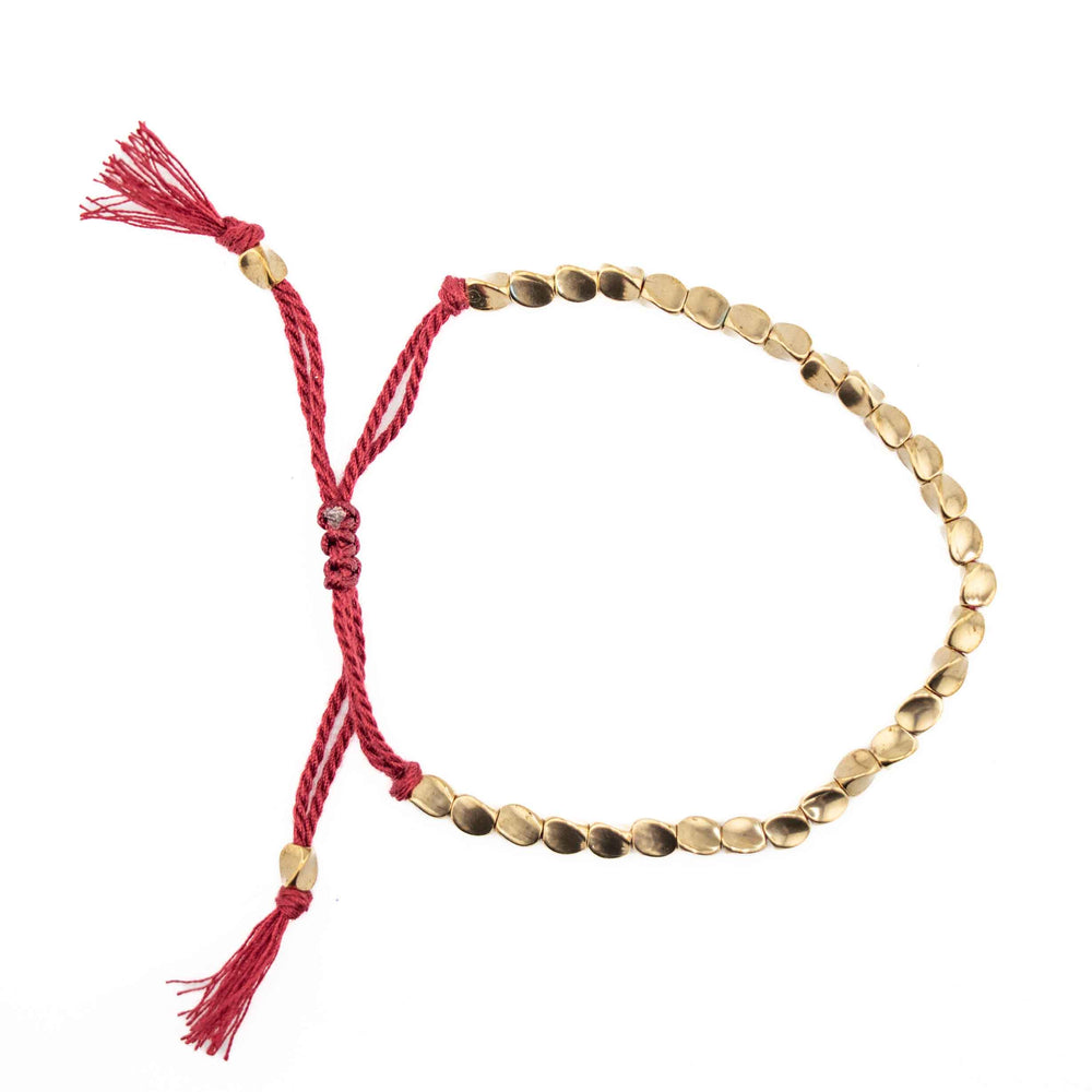 An adjustable bracelet featuring organic shaped gold copper beads on a red braided cord with a sliding knot closure and tassel ends.