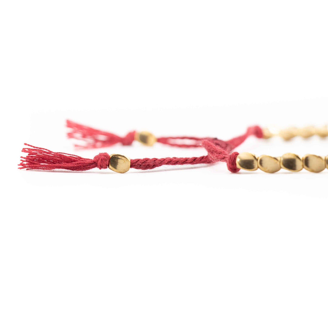 A close up, low angle shot of the red braided cord and gold copper beads, highlighting the tassel ends and sliding knot detail.