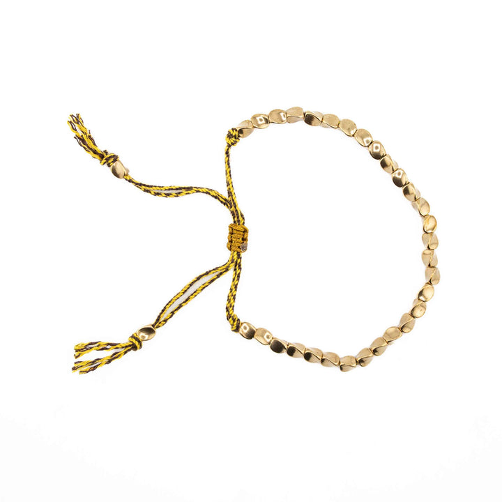 An adjustable bracelet featuring organic-shaped gold copper beads on a yellow braided cord with a sliding knot closure and tassel ends.