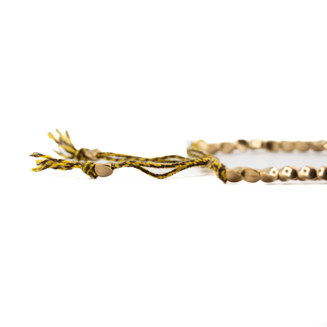 A close-up, low-angle shot of the yellow braided cord and gold copper beads, highlighting the tassel ends and sliding knot detail.