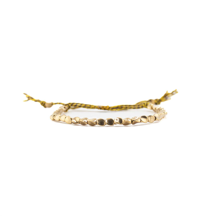 A horizontal, eye-level view of the copper bead bracelet, focusing on the row of shiny, organic-shaped gold beads with the yellow cord and tassels blurred in the background.