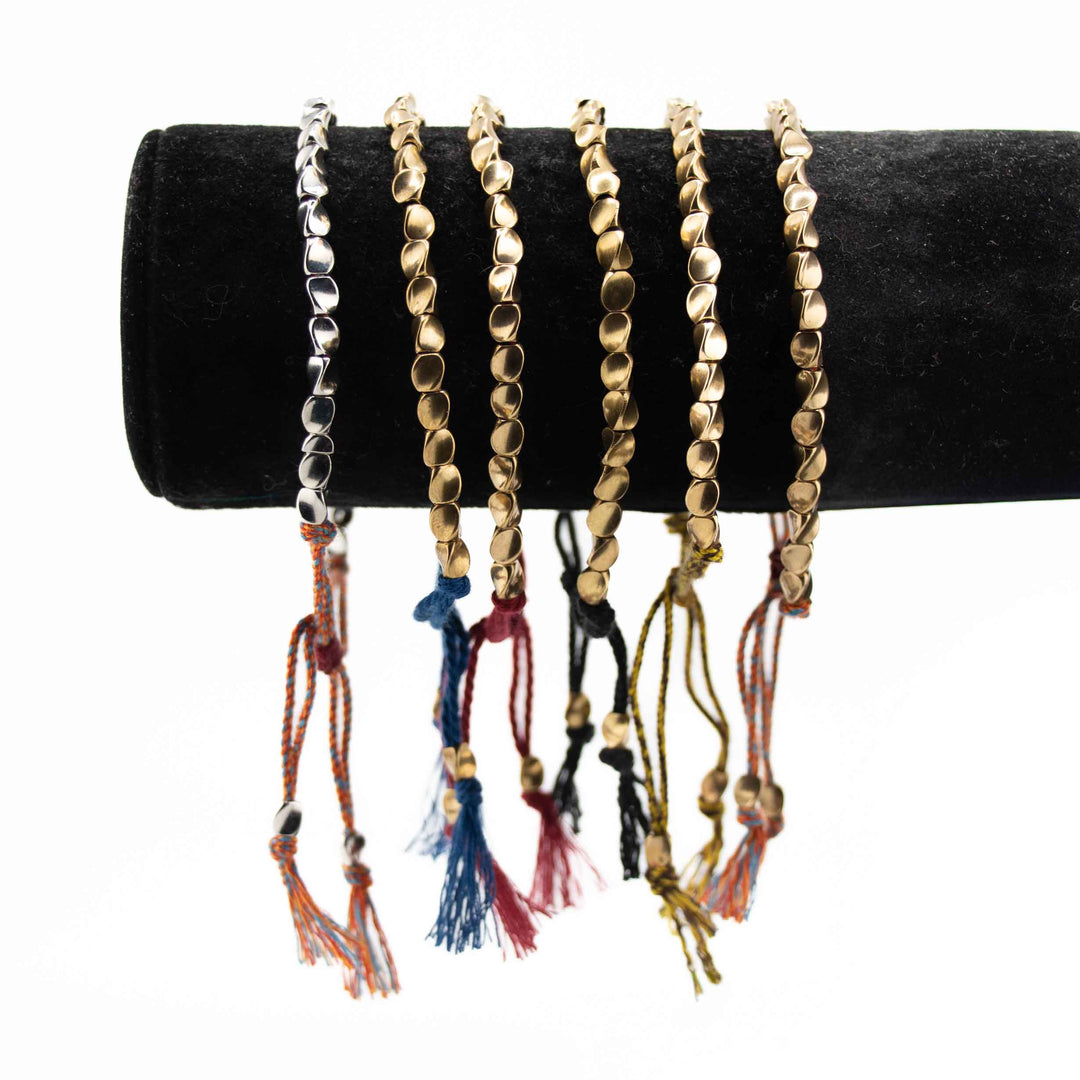 A group of five adjustable copper bead bracelets in various cord colors—red, yellow, black, and multi-colored—arranged together on a white background.