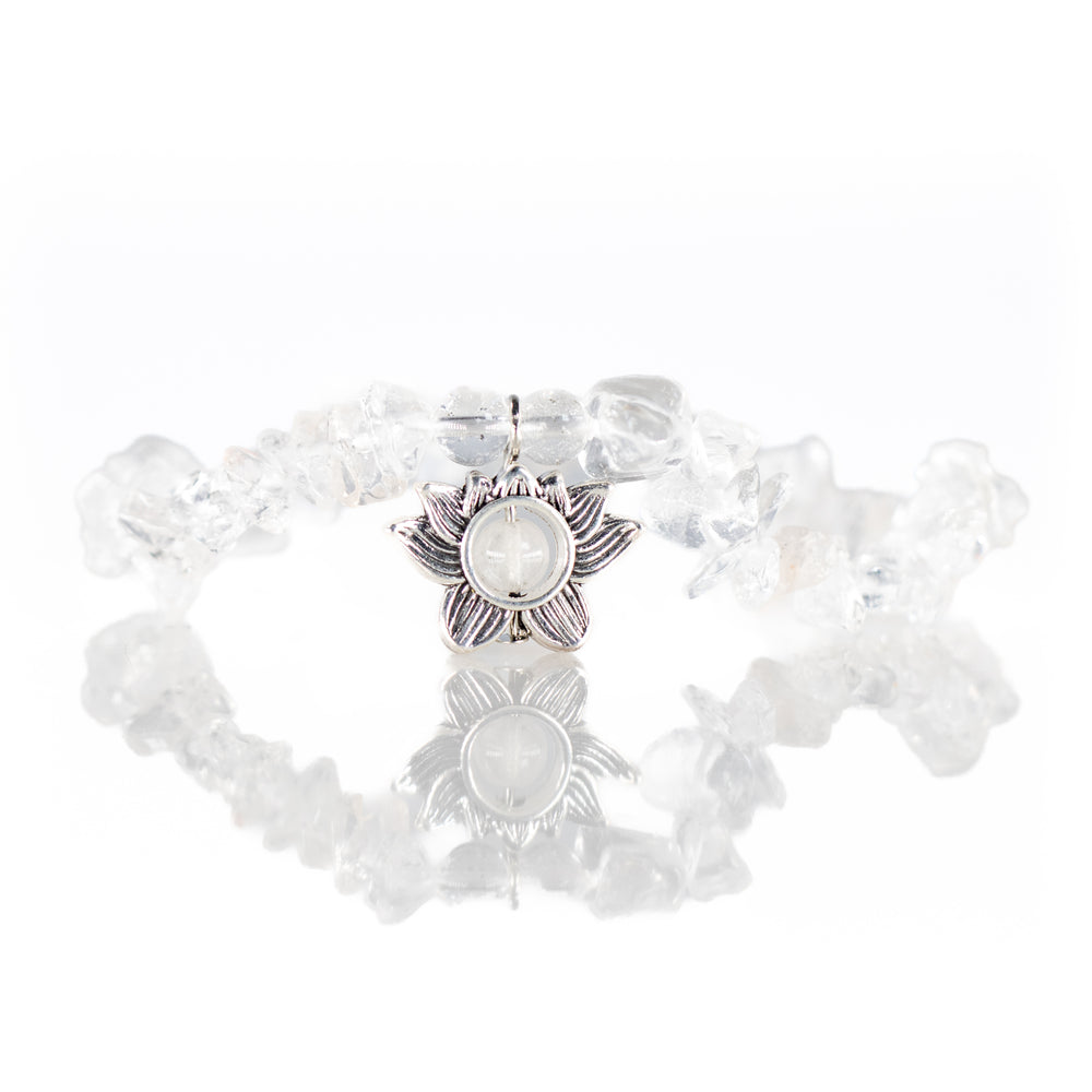 A clear quartz chip bracelet with a central silver-toned lotus flower charm reflected on a white glossy surface
