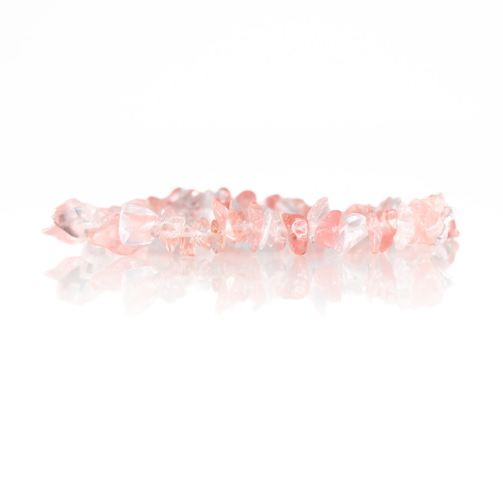 A rose quartz chip bead bracelet made of irregular polished translucent pale pink stones reflected on a pristine white surface