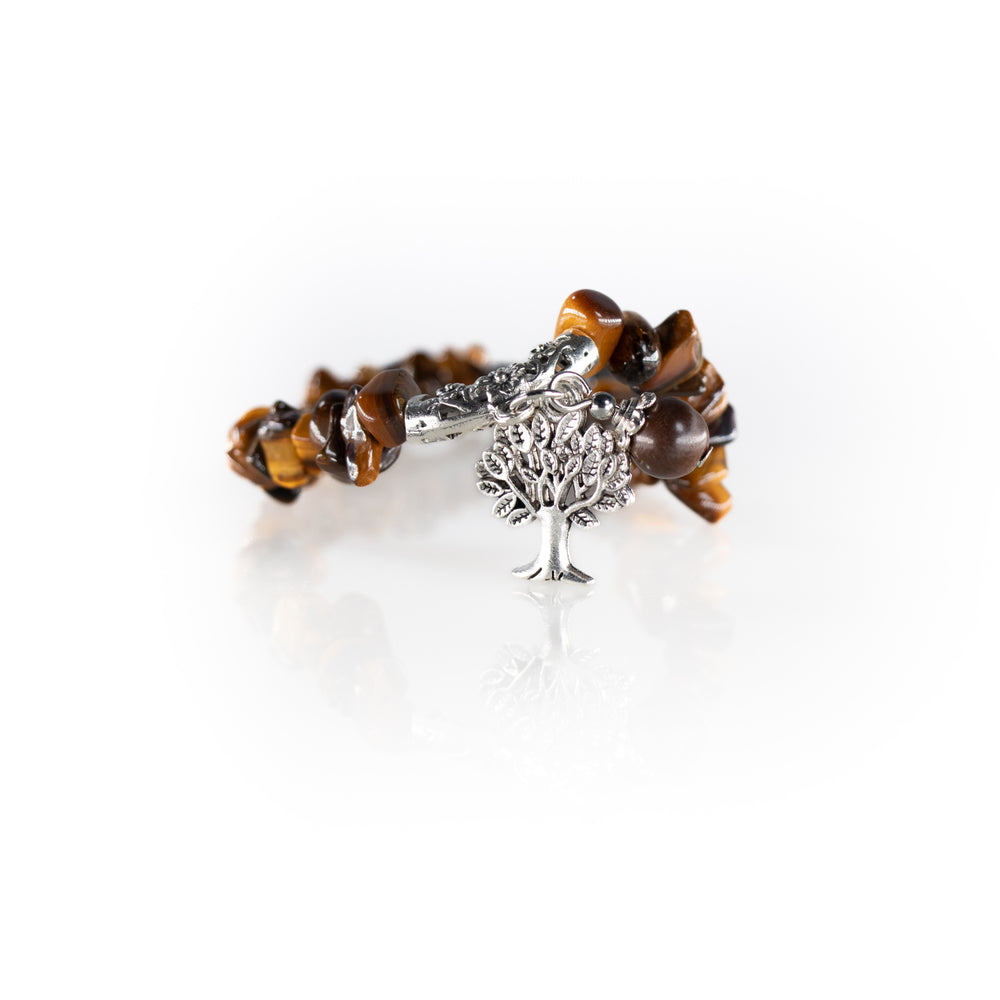 A tiger's eye chip bead bracelet featuring a silver tree of life charm and an ornate silver toggle clasp rests on a reflective white surface