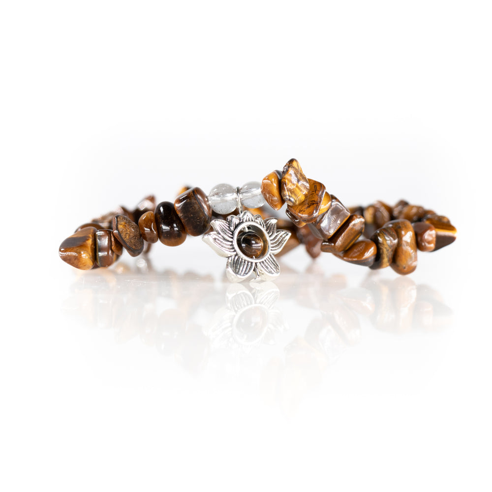 A brown and golden-brown Tiger's Eye chip bead bracelet featuring a silver-toned flower charm and two clear glass beads reflecting on a white studio background
