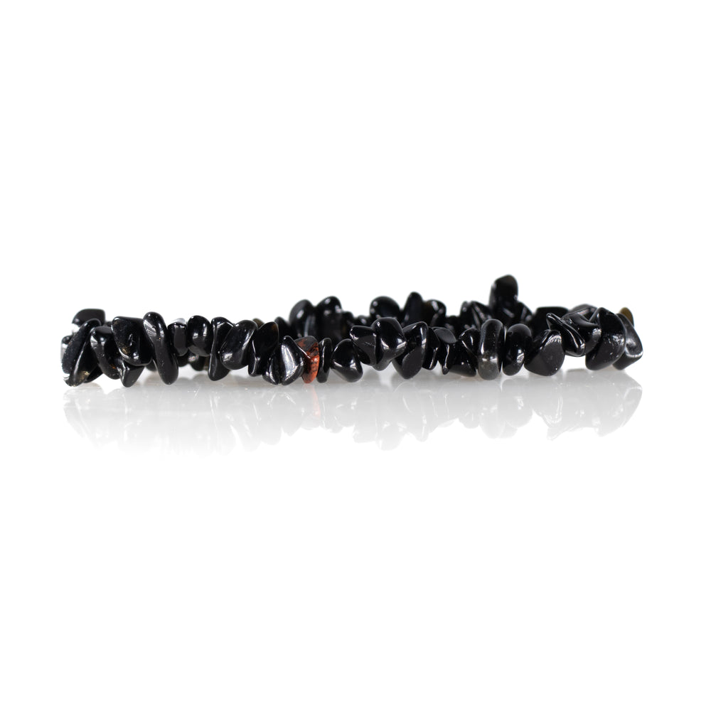 A black onyx gemstone bracelet with irregularly shaped polished stones and one distinctive reddish-brown bead resting on a reflective white surface