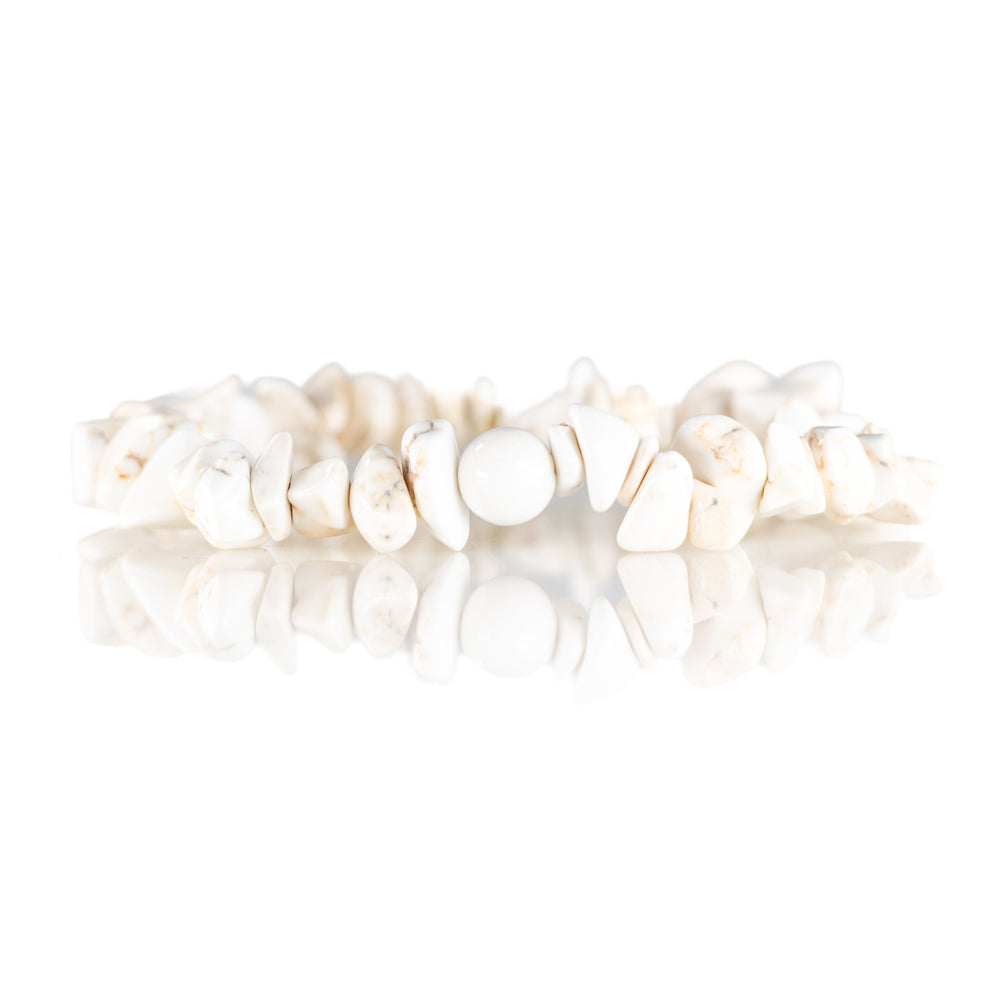 Photograph of a white Howlite gemstone bracelet featuring irregular tumbled chip beads and a smooth round central bead with subtle natural tan veining on a reflective white surface