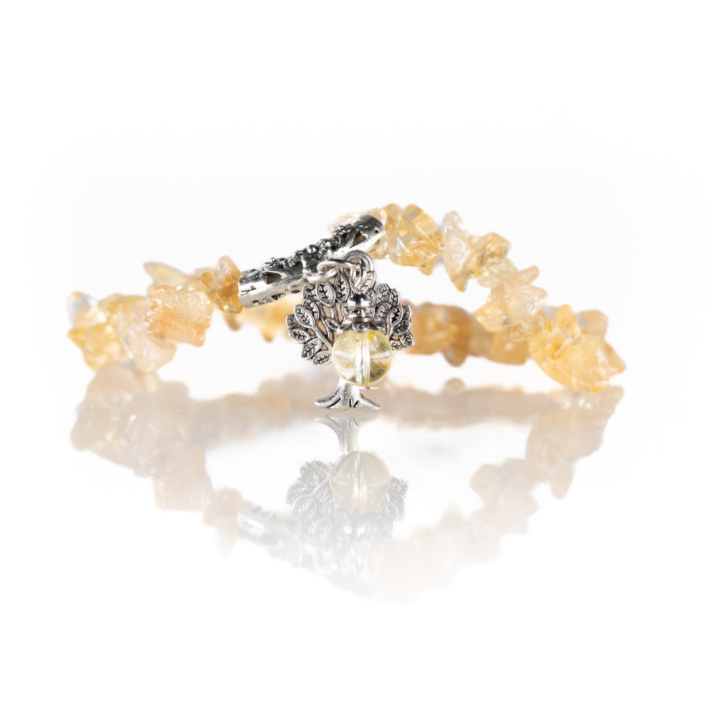 Photograph of a handmade bracelet with pale yellow citrine chip beads, an intricate silver-toned tree of life charm, and a decorative silver toggle clasp reflecting on a white studio surface