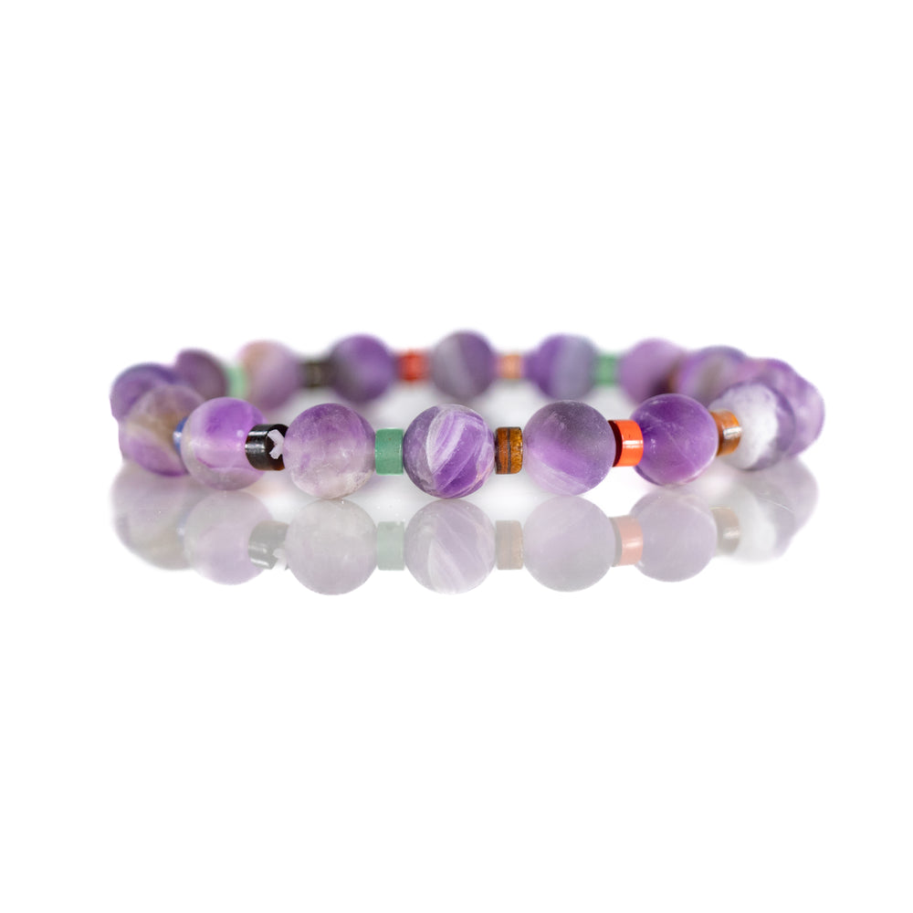 Photograph of a purple beaded bracelet featuring varied shades of polished amethyst beads interspersed with small green and orange spacer beads on a reflective white surface