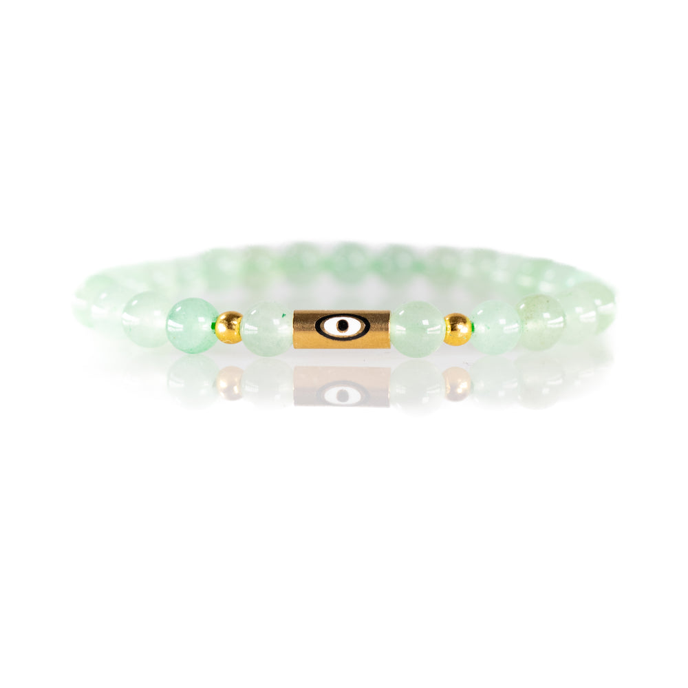 Jewelry light green beaded bracelet featuring a central gold cylindrical evil eye charm flanked by two small gold accent beads on a reflective white surface