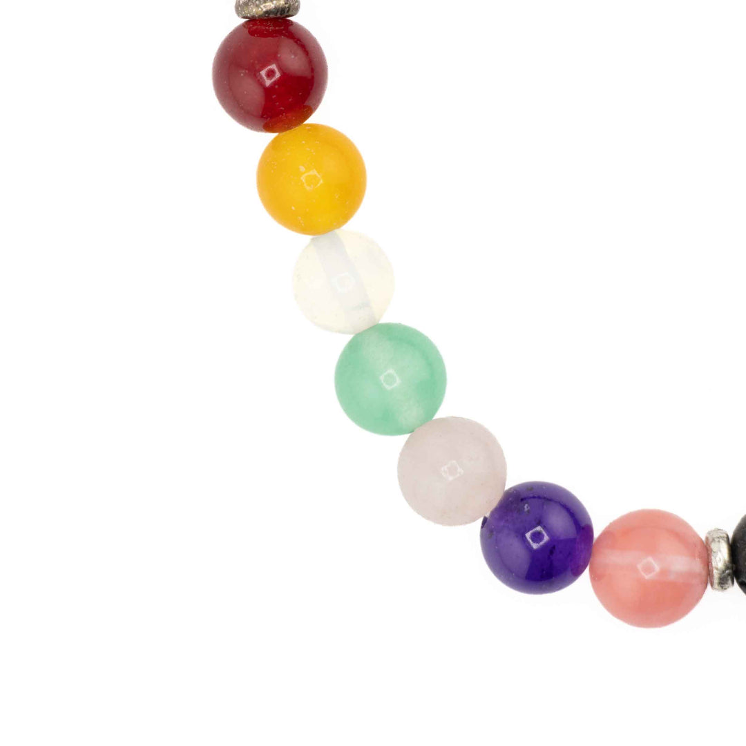 Detailed view of seven colorful chakra gemstone beads in red, yellow, clear, green, light pink, purple, and dark pink on a beaded stretch bracelet