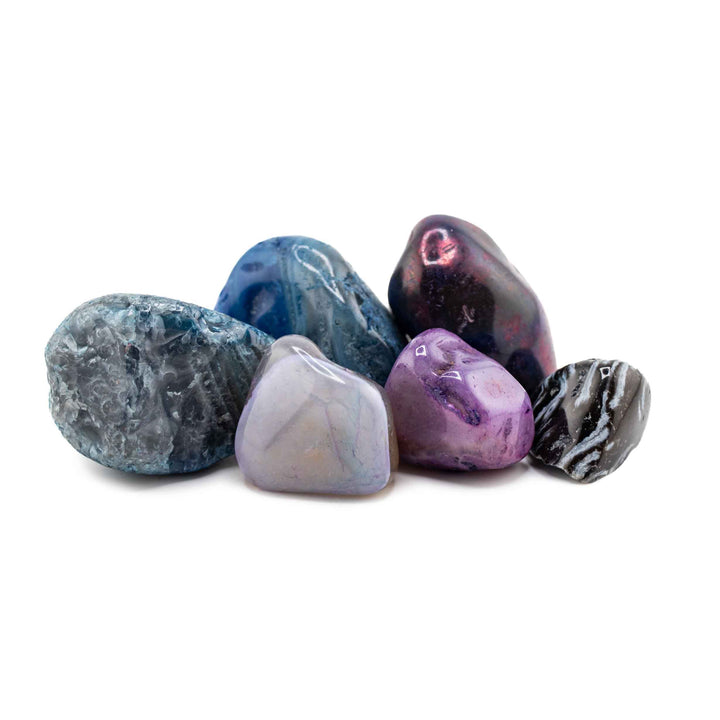 A small cluster of six dyed and banded agate tumbled stones grouped together against a plain white backdrop.