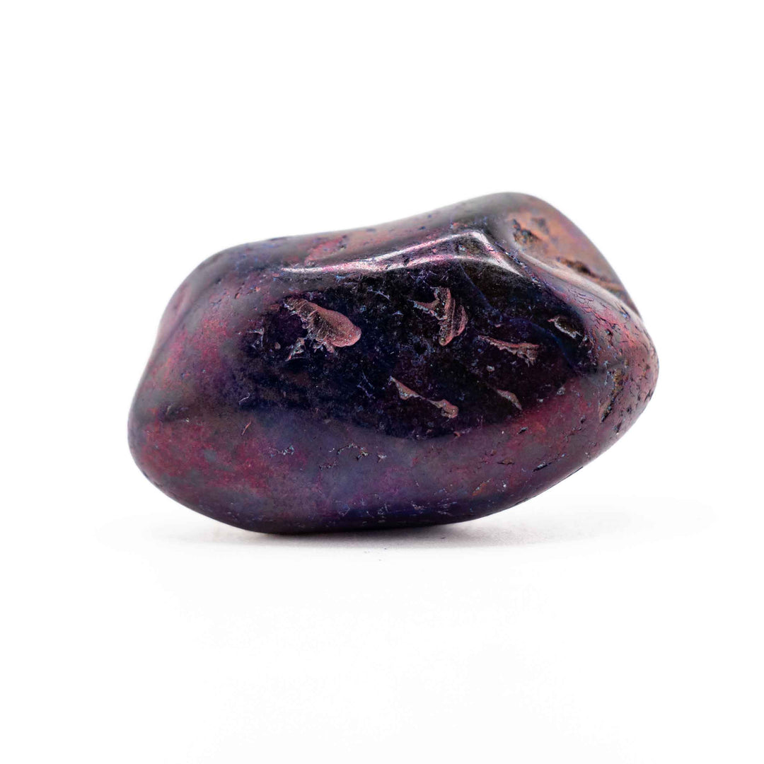 A smooth, dark purple dyed agate tumbled stone positioned horizontally in the center of a white backdrop.