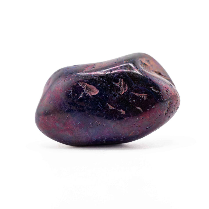 A smooth, dark purple dyed agate tumbled stone positioned horizontally in the center of a white backdrop.