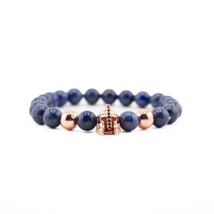 A close-up, low-angle shot of a Lapis Lazuli gemstone bracelet, highlighting the polished deep blue beads and a gold-colored ancient helmet accent.