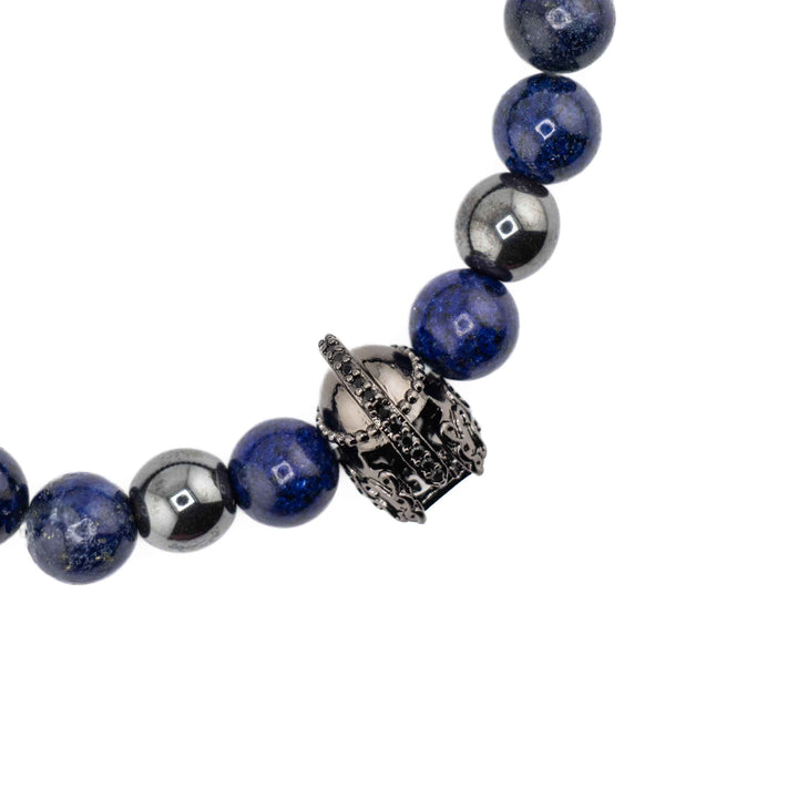 An angled, eye-level view of a Lapis Lazuli gemstone bracelet, highlighting the contrast between the matte deep blue beads and the polished gold-colored helmet accent.