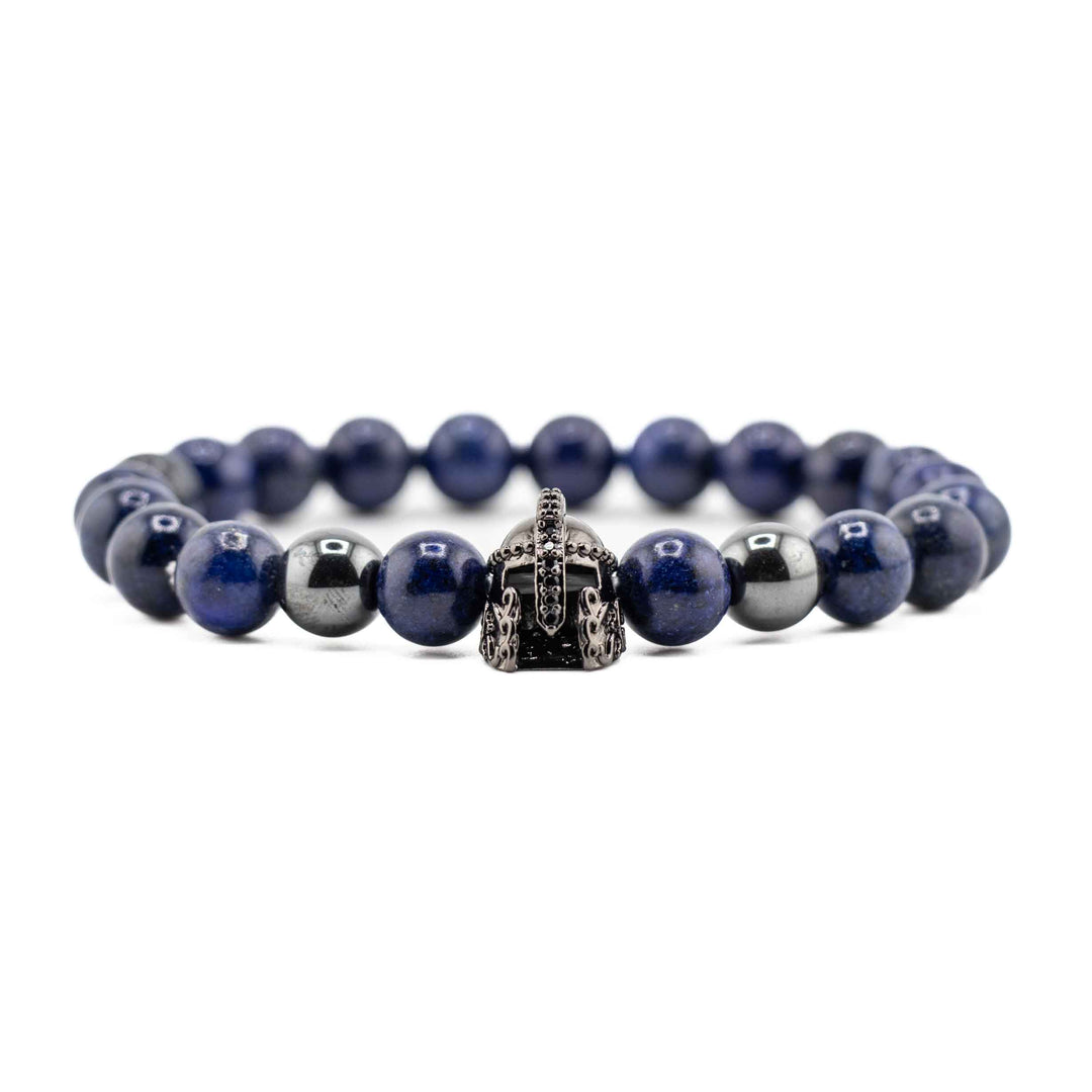 A close-up shot of several deep blue Lapis Lazuli beads and the gold-colored ancient helmet accent, showing the natural stone texture and metallic detail.