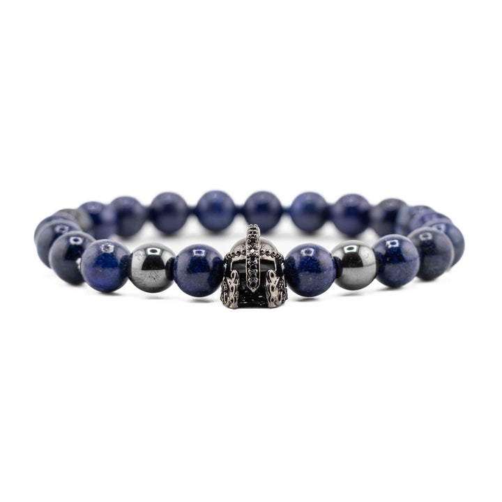 A close-up shot of several deep blue Lapis Lazuli beads and the gold-colored ancient helmet accent, showing the natural stone texture and metallic detail.