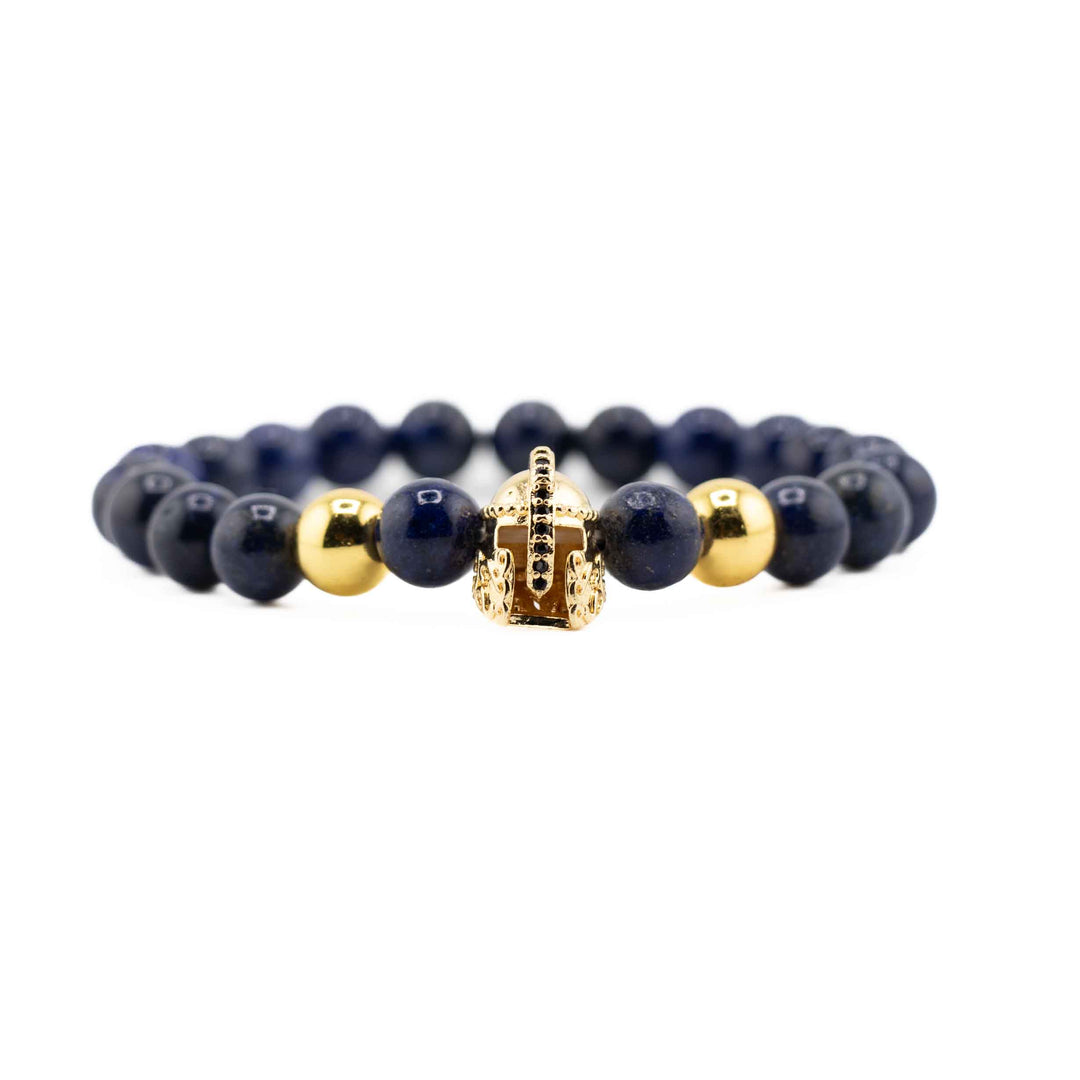 A high-angle shot of a Lapis Lazuli gemstone bracelet, showing the full circle of deep blue beads and the gold-colored ancient helmet accent on a white background.