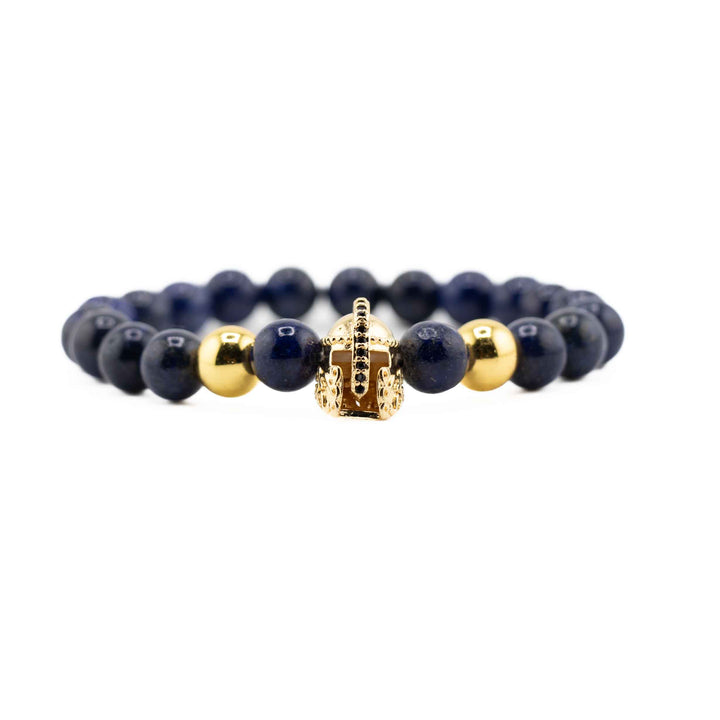 A high-angle shot of a Lapis Lazuli gemstone bracelet, showing the full circle of deep blue beads and the gold-colored ancient helmet accent on a white background.