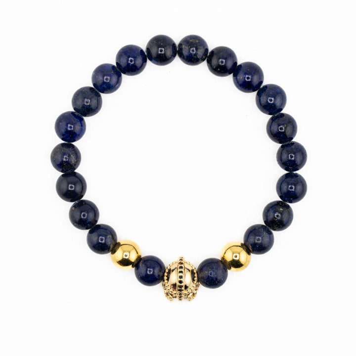 A group of three Natural Lapis Lazuli gemstone bracelets, each featuring a unique gold-colored accent—an ancient helmet, a textured barrel bead, and a simple spacer—displayed together on a white background.