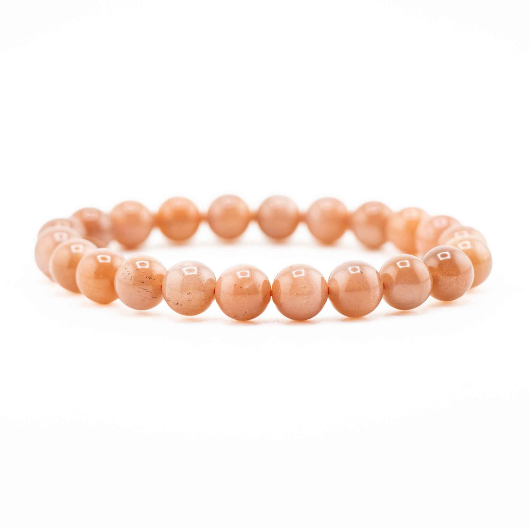Side view resting shot of a Peach Moonstone gemstone beaded bracelet resting flat on a white background