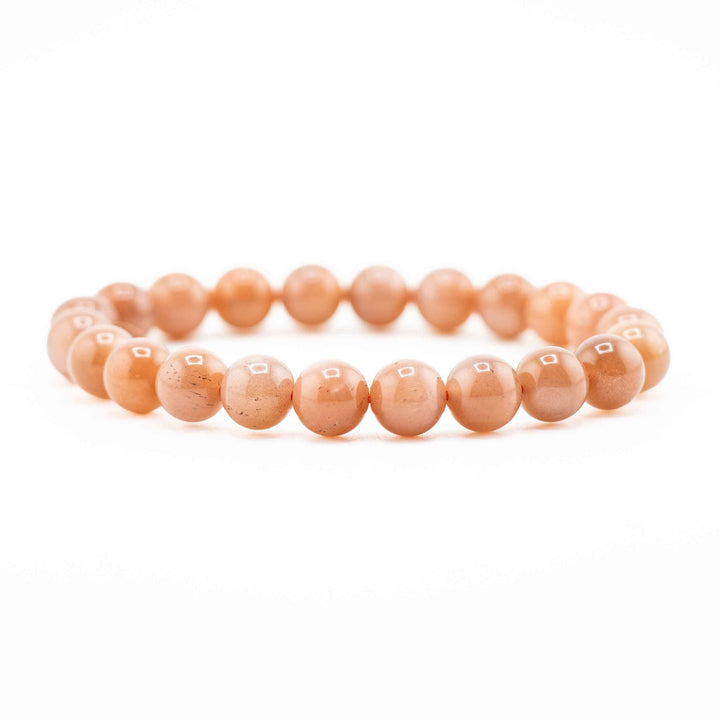Side view resting shot of a Peach Moonstone gemstone beaded bracelet resting flat on a white background