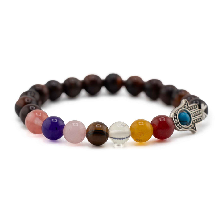 Side view resting shot displaying colorful chakra beads in pink, purple, clear, yellow, and red alongside a silver Hamsa hand charm on a red Tiger Eye stretch bracelet