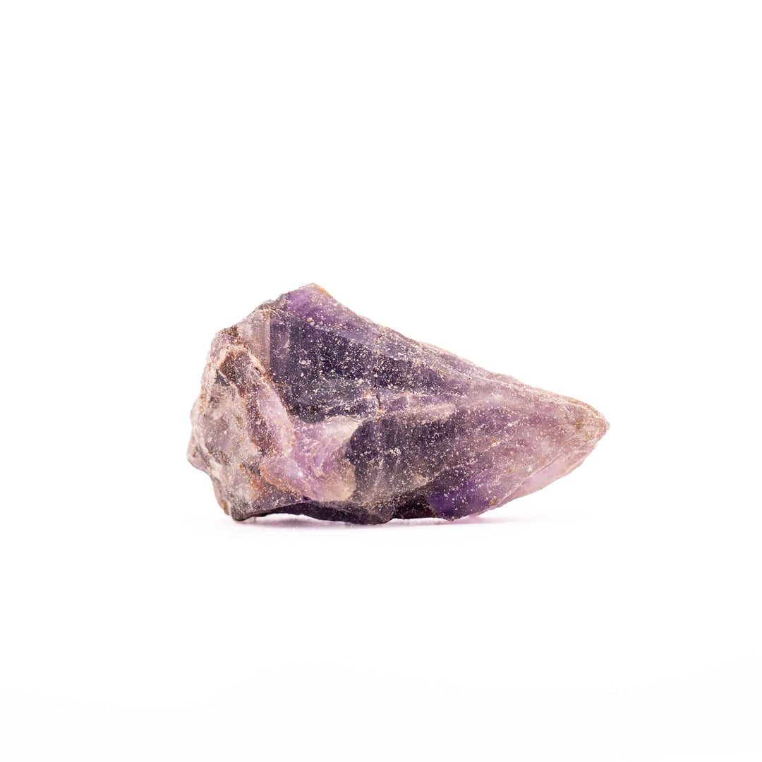 A rough, unpolished piece of purple amethyst crystal with natural facets and a textured, earthy base, photographed on a seamless white background.