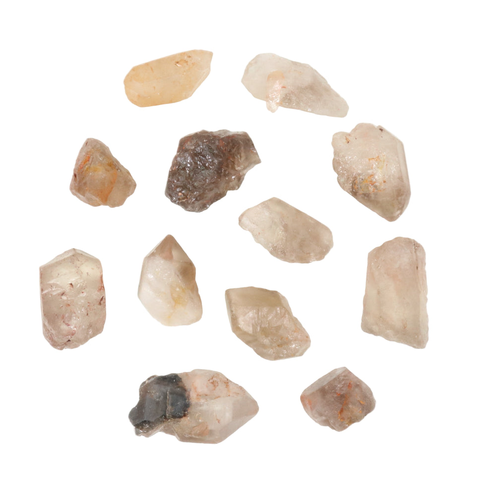 Photograph of a scattered group of naturally formed rough quartz crystals featuring varied clear, milky, and smoky hues with visible reddish-brown inclusions