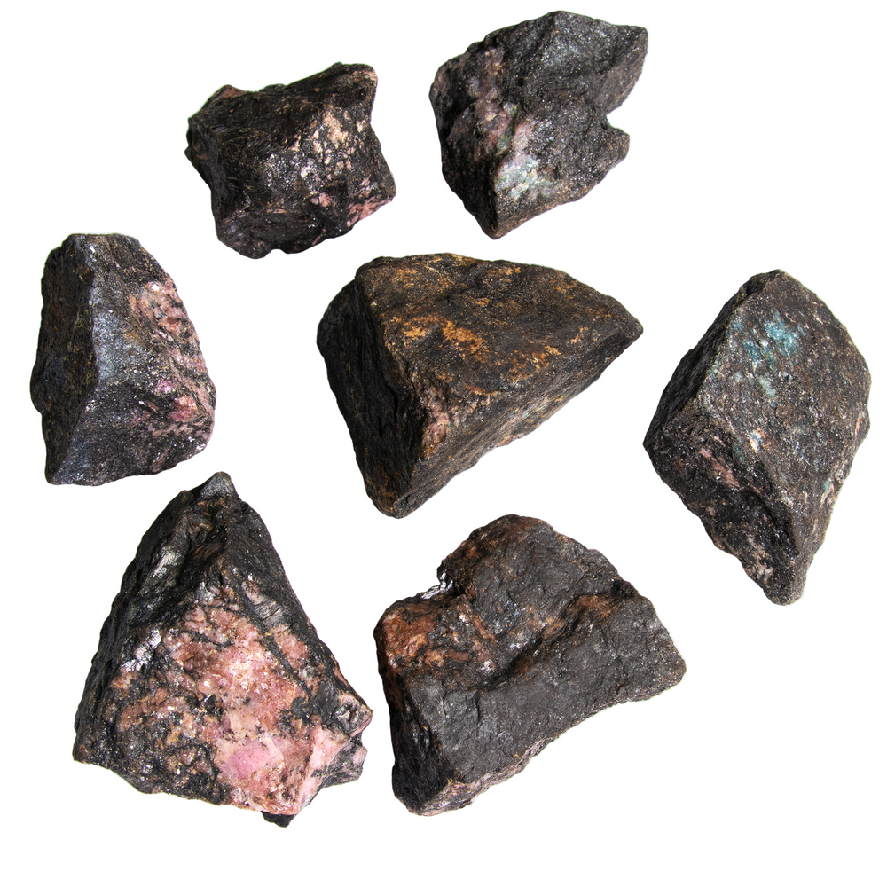 Photograph of seven unpolished mineral specimens showing dark gray matrix with vibrant pink, reddish-brown, and greenish-blue inclusions and glistening crystalline textures